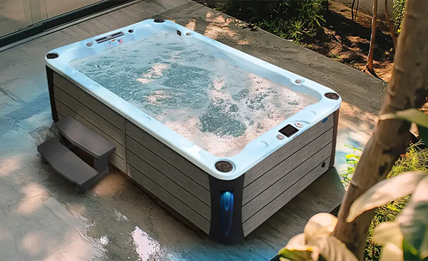 An overhead view of a Cal Spas Deck hot tub with blue corner lights and 30-inch steps on a wooden, wooded patio.